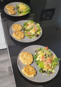 3 plates of salmon patties and lettuce and vegetable salad on plates on the counter